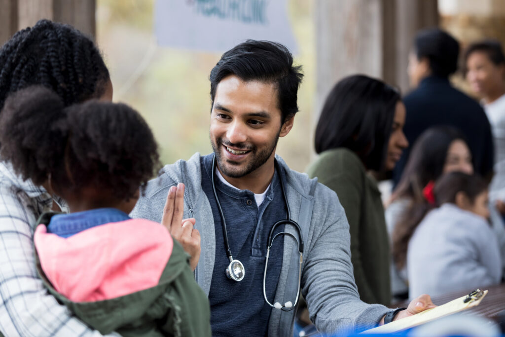 Community Health Worker holds up two fingers as he checks a young girl's vision. The girl and her mom are visiting an outdoor free clinic.